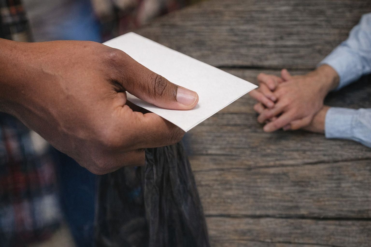 En hånd som overleverer en hvit konvolutt over et rustikk trebord.
